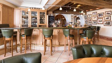 A stylish bar with wooden shelves and cozy green chairs. Frames with many photos hang on the walls.