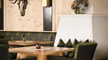 A stylish restaurant interior with wooden paneling and cozy seating. On the wall hangs a deer antler and a decorative wreath design.