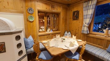 Eine gemütliche Sitzecke in einem Holz-interior mit einem runden Tisch. An den Wänden hängen dekorative Teller und ein Fenster lässt Licht herein.
