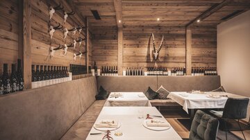 A modern restaurant with wooden walls and elegant tables. Bottles and decorative elements made of natural materials can be seen on the wall.
