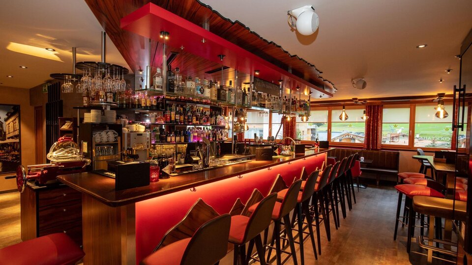 Eine moderne Bar mit einer einladenden Einsatz von rotem Licht. Die Theke ist gut bestückt und es gibt viele Stühle, die auf Gäste warten.