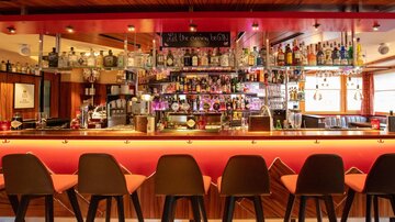 Eine stilvolle Bar mit einer langen Theke und modernen Barhockern. Im Hintergrund sind viele alkoholische Getränke in Regal präsentiert.