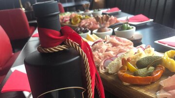 Ein elegant gedeckter Tisch mit einer Auswahl an Fleischplatten und Beilagen. Im Vordergrund steht eine Flasche Kiwi Gin mit einer roten Schleife.