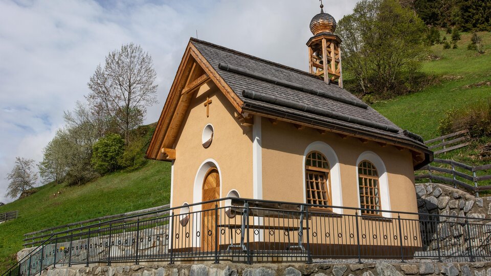 Eine kleine Kapelle auf einem sanften Hügel umgeben von Bäumen. Der Himmel ist teilweise bewölkt, und die Architektur ist schlicht und charmant. | © Bernhard Gruber – Photography