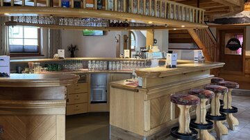 A cozy wooden bar with several stools and a well-stocked shelf. The ambiance is warm and inviting.