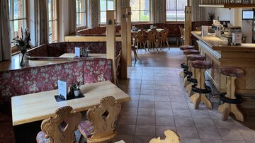 A cozy restaurant with wooden furniture and blooming seating areas. Large windows provide plenty of daylight and an inviting atmosphere.