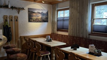 A cozy dining room with wooden tables and chairs. A picture of a mountain landscape hangs on the wall.