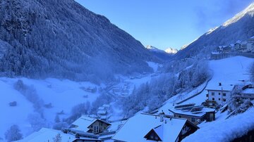 A snow-covered mountain landscape with small, quiet houses. The sky is clear and blue, and the scenery exudes a peaceful winter atmosphere.