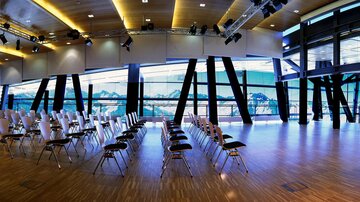 A modern event room with white chairs in rows. Large windows offer a view of the landscape.