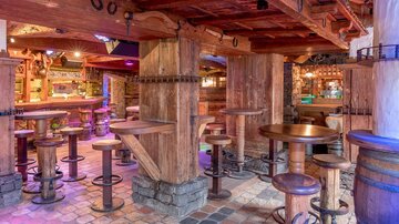 Eine gemütliche Bar mit Holzvertäfelungen und mehreren Stehtischen. Die Einrichtung vermittelt eine rustikale Atmosphäre.