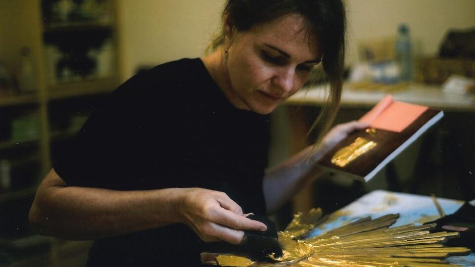 An artist is working on a gold-colored, star-shaped sculpture. She is holding a book in her hand and concentrating on her creative activity.