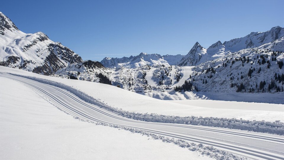 A snowy mountain landscape under a clear blue sky. Ski tracks lead through the untouched snow cover.