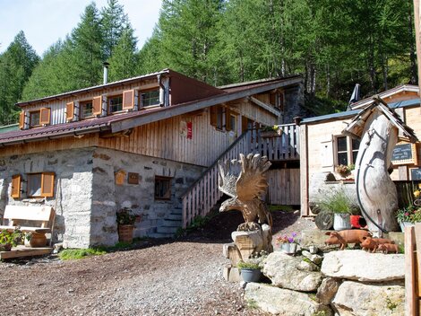 Ein gemütliches Holzhaus in den Bergen, umgeben von grünen Bäumen. Vor dem Haus steht eine dekorative Skulptur.