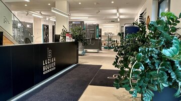 A modern reception area with a dark reception counter.  
Plants and bright light create an inviting atmosphere.