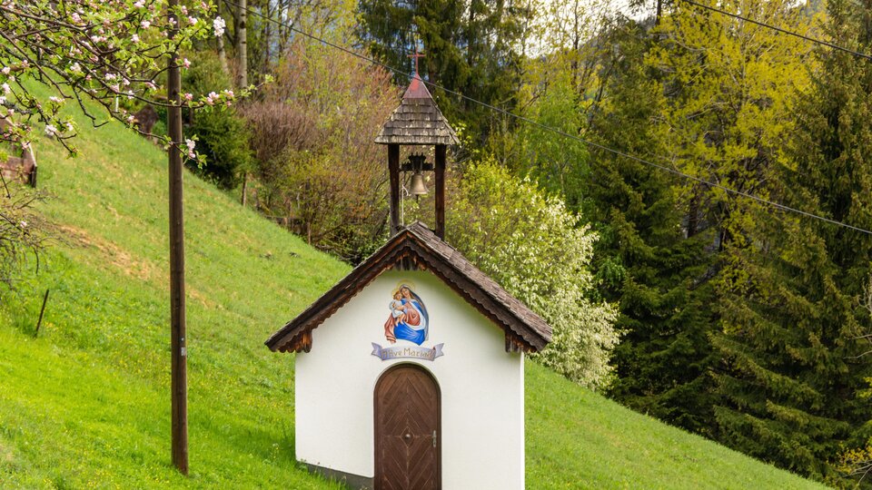 Eine kleine Kapelle steht auf einer grünen Wiese. Umgeben von Bäumen vermittelt sie eine ruhige und idyllische Atmosphäre.