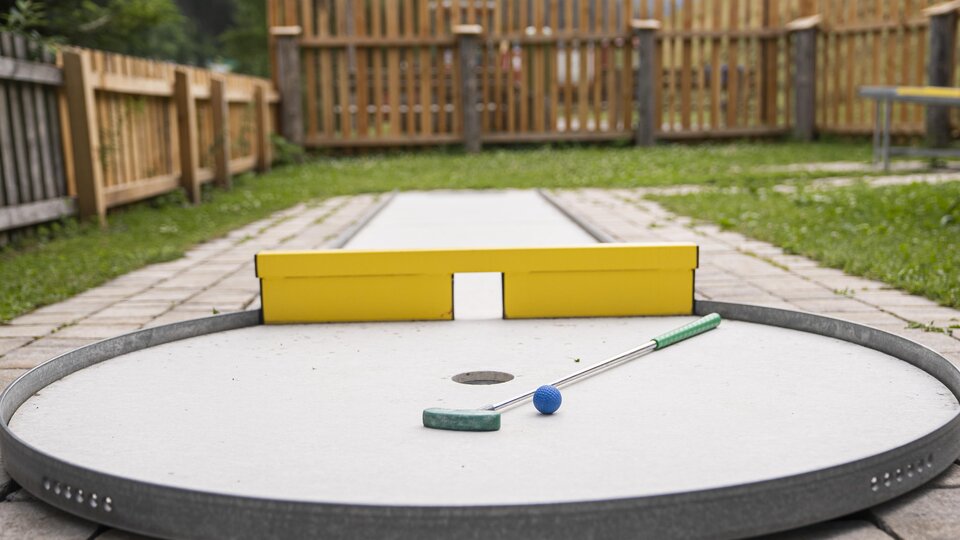 A mini golf course with a round playing area and a yellow target wall. The ball and the club are ready to play.