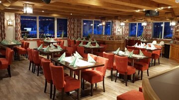 Ein gemütliches Restaurant mit roten Stühlen und grünen Servietten auf den Tischen. Die großen Fenster bieten einen Blick auf die Umgebung.