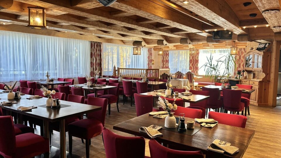 Ein gemütliches Restaurant mit Holzelementen und roten Stühlen. Die Tische sind freundlich gedeckt und die Fenster bieten einen Blick nach draußen.