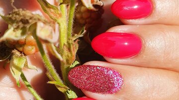 Helle rote Nägel mit Glitzer auf einem Finger, die eine Pflanze mit Brombeeren halten. Der Hintergrund zeigt grüne Blätter.