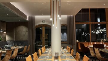Ein elegantes Restaurant mit einem langen Holztisch und stilvollen Stühlen. Die Beleuchtung sorgt für eine gemütliche Atmosphäre.