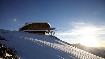 Eine moderne Bergstation in einer schneebedeckten Landschaft. Die Sonne geht hinter den Bergen auf und sorgt für eine malerische Aussicht.