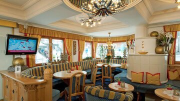 Ein gemütliches Restaurant mit blauen und gelben Stoffen. Helle Fenster und eine dekorative Decke schaffen eine einladende Atmosphäre.