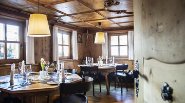 Ein gemütliches Restaurant mit Holzwänden und großen Fenstern. Der Tisch ist liebevoll gedeckt und es hängen lampen von der Decke.