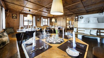 Ein gemütliches Restaurant mit Holzwänden und warmem Licht. Die Tische sind elegant gedeckt und laden zum Essen ein.