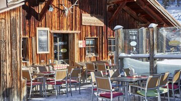 Ein gemütliches Restaurant mit Holzfassade und Außenbereich. Es gibt mehrere Tische auf schneebedecktem Boden.