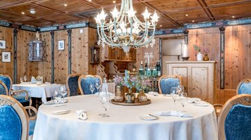 Ein elegantes Restaurant mit einem runden Tisch und blauen Stühlen. Über dem Tisch hängt ein funkelnder Kronleuchter in einem mit Holz verkleideten Raum.