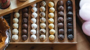 Eine Auswahl an köstlichen Pralinen in verschiedenen Geschmacksrichtungen. Die Pralinen sind ordentlich auf einem Holzbrett angeordnet.