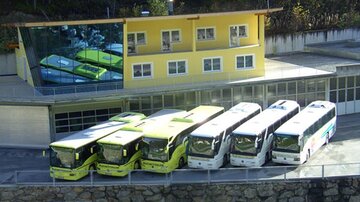 Eine moderne Haltestelle mit mehreren Bussen in gelb und weiß. Im Hintergrund ist ein gelbes Gebäude mit großen Fenstern zu sehen.