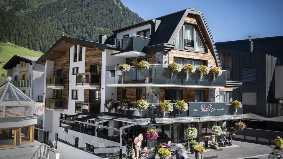 A modern hotel with blooming balcony plants in a mountain landscape. The facade is friendly and inviting.