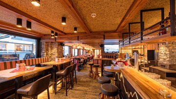 A cozy bar with wooden interiors and warm lighting. The seating invites relaxation and enjoyment.
