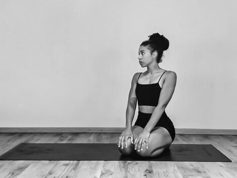 A person is sitting in a yoga position on a mat. The room is simple and minimalistic.