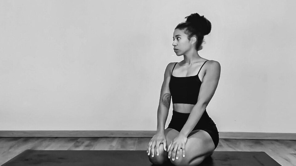 A person is sitting in a yoga position on a mat. The room is simple and minimalistic.
