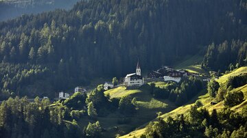 A picturesque mountain landscape with a small village and a church. Surrounded by dense forests and green meadows.