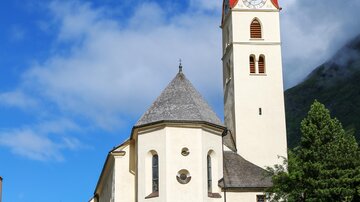 A beautiful church with a red tower and a white facade. In the foreground, there is a modern building with a glass section.