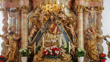 A magnificent altar with a statue of the Madonna, surrounded by angels and floral decorations. The golden embellishments and the detailed representation create a festive atmosphere.