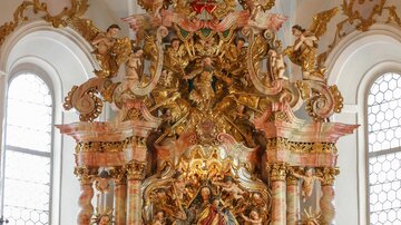 A magnificent altar in a church, richly decorated with gold and statues. Flowers adorn the altar, creating a festive atmosphere.