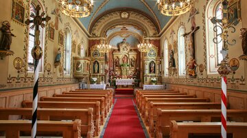 A beautiful church with wooden benches and a red carpet in the center. The walls are artistically decorated with religious images.