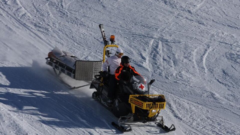 Ein Schneemobil fährt über den Schnee. Auf dem Schneemobil sind zwei Personen, die Ausrüstung für medizinische Notfälle transportieren.