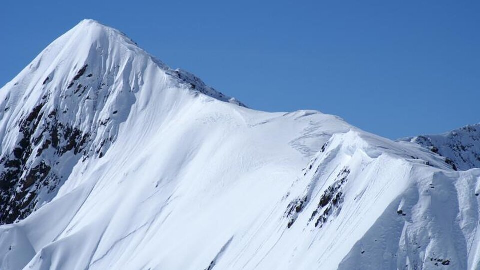 Ein schneebedeckter Berg unter einem klaren blauen Himmel. Die Landschaft ist majestätisch und beeindruckend.