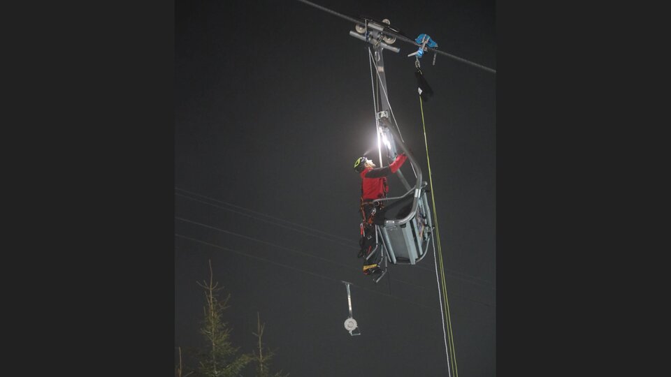 A person is working on a cable car at night. They are wearing safety gear and using a flashlight.