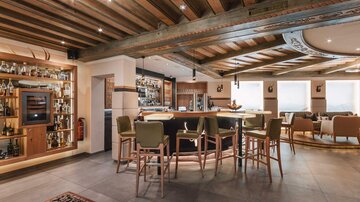 Eine elegante Bar mit Holzdecke und moderner Einrichtung. Gemütliche Sitze und ein gut bestücktes Regal verleihen der Atmosphäre einen einladenden Charakter.