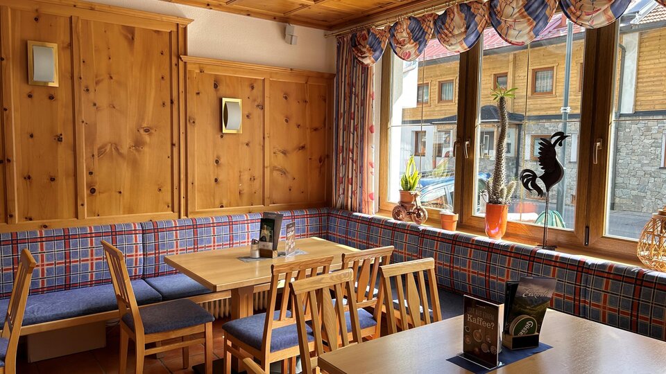 Ein gemütliches Restaurant mit Holzmöbeln und karierten Polstern. Große Fenster lassen viel Licht herein und bieten einen Blick nach draußen.