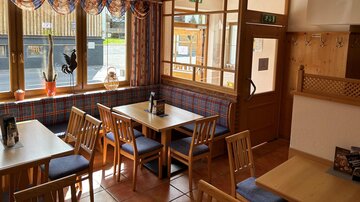 Ein gemütliches Restaurant mit Holzmöbeln und großen Fenstern. Der Raum ist hell und einladend, ideal für gesellige Gespräche.