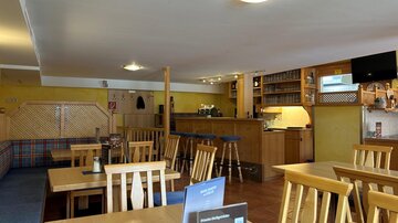 Ein gemütliches Restaurant mit Holztischen und Stühlen. Die Bar ist gut sichtbar und die Wände sind in warmen Farben gestrichen.