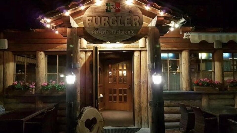 Ein rustikales Restaurant aus Holz mit einer einladenden Fassade und warmem Licht. Die Eingangstür ist aus Holz und die Fenster sind mit blühenden Pflanzen geschmückt.