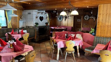 Ein gemütliches Restaurant mit Holzwänden und rustikalen Möbeln. Die Tische sind mit roten Tischdecken dekoriert und gut vorbereitet.